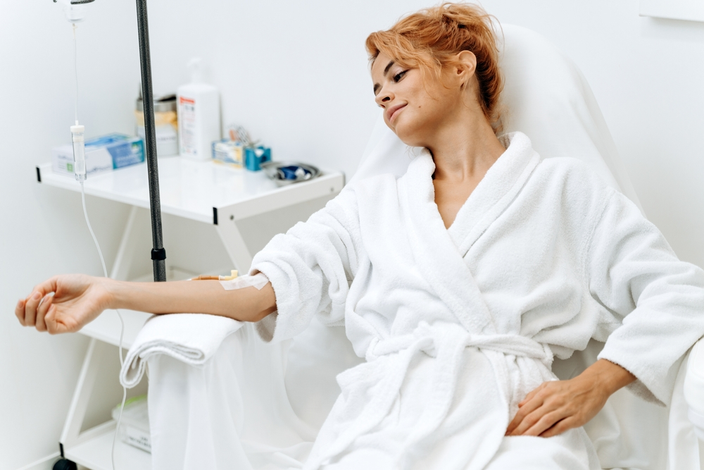 woman sitting in armchair and closed eyes while receiving IV therapy treatment