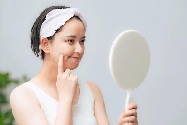 Concerned woman examining skin in mirror, highlighting side effects and risks of Juvederm Vollure XC treatment