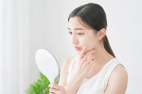 Concerned woman examining her face in a mirror, representing possible side effects and risks of Restylane Defyne treatment
